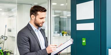 Chloee Uddain checking a cleaning schedule beside a commercial office entrance